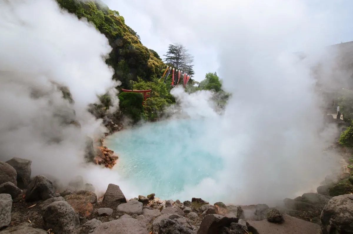 Manantial de aguas termales humeante de color turquesa con un torii en Hakone