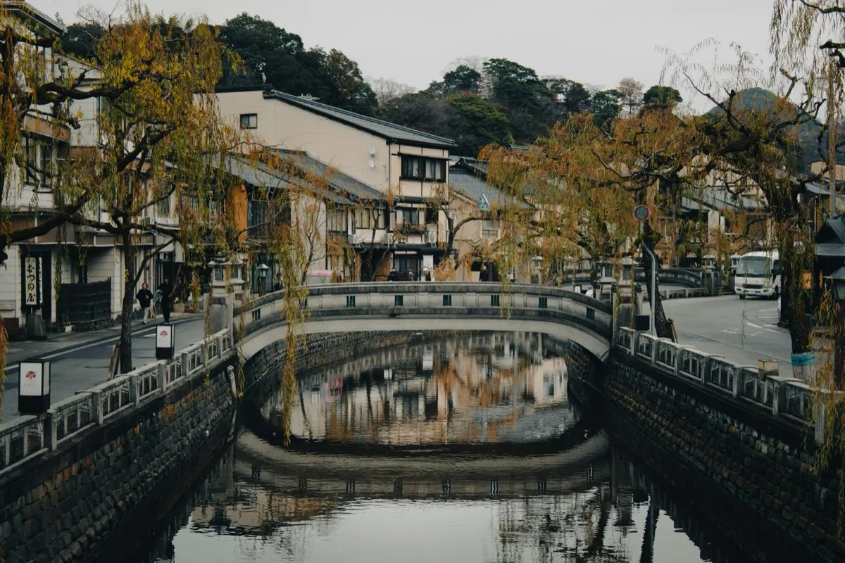 Canal de Kinosaki con un puente de piedra y sauces reflejados en el agua