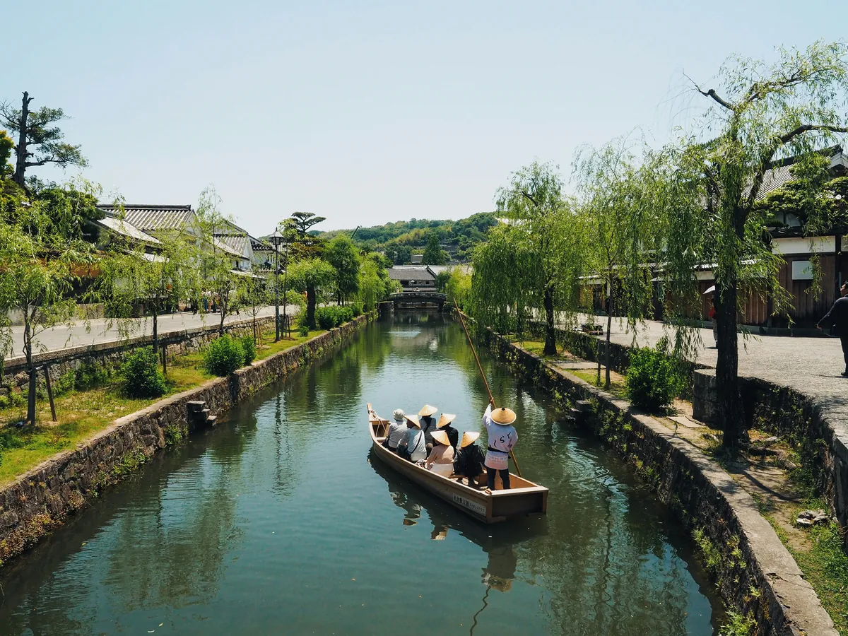 Barca tradicional con pasajeros recorriendo el canal del barrio de Bikan entre sauces, en Kurashiki