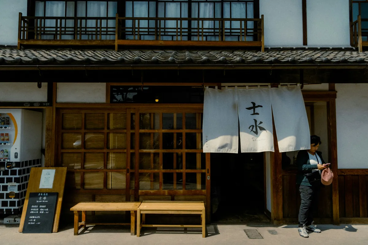 Fachada tradicional de madera y muro blanco con un noren colgado, en una calle del barrio de Bikan de Kurashiki
