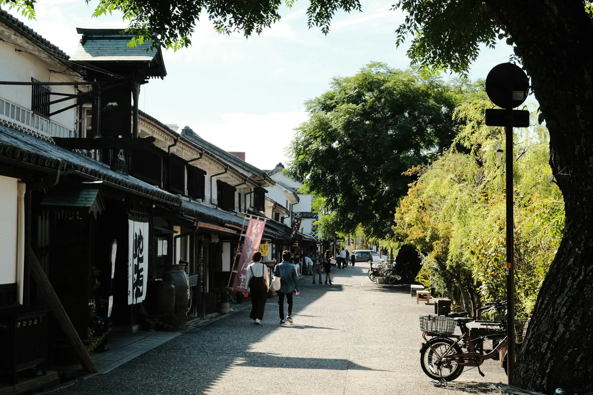 Calle de almacenes blancos de época Edo con viandantes y un sauce, en el barrio de Bikan de Kurashiki