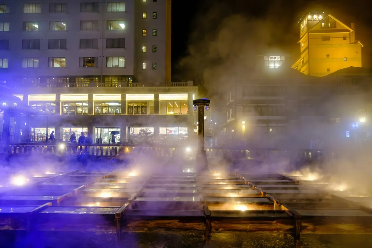 Canales de madera iluminados del Yubatake con vapor en Kusatsu de noche