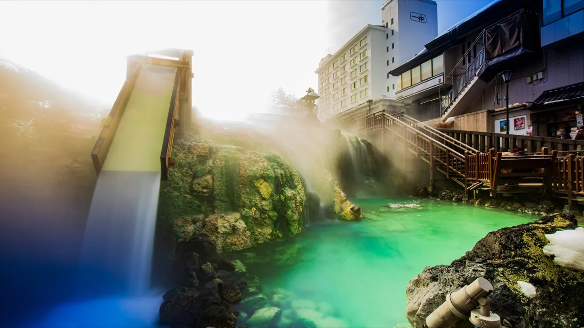 Aguas termales verdes y rampa de madera de enfriado del Yubatake en Kusatsu