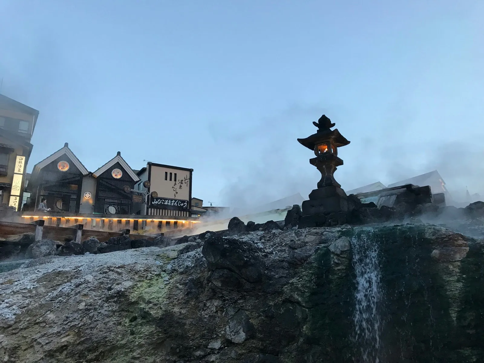 Campo de aguas termales Yubatake humeante con una linterna de piedra en Kusatsu Onsen