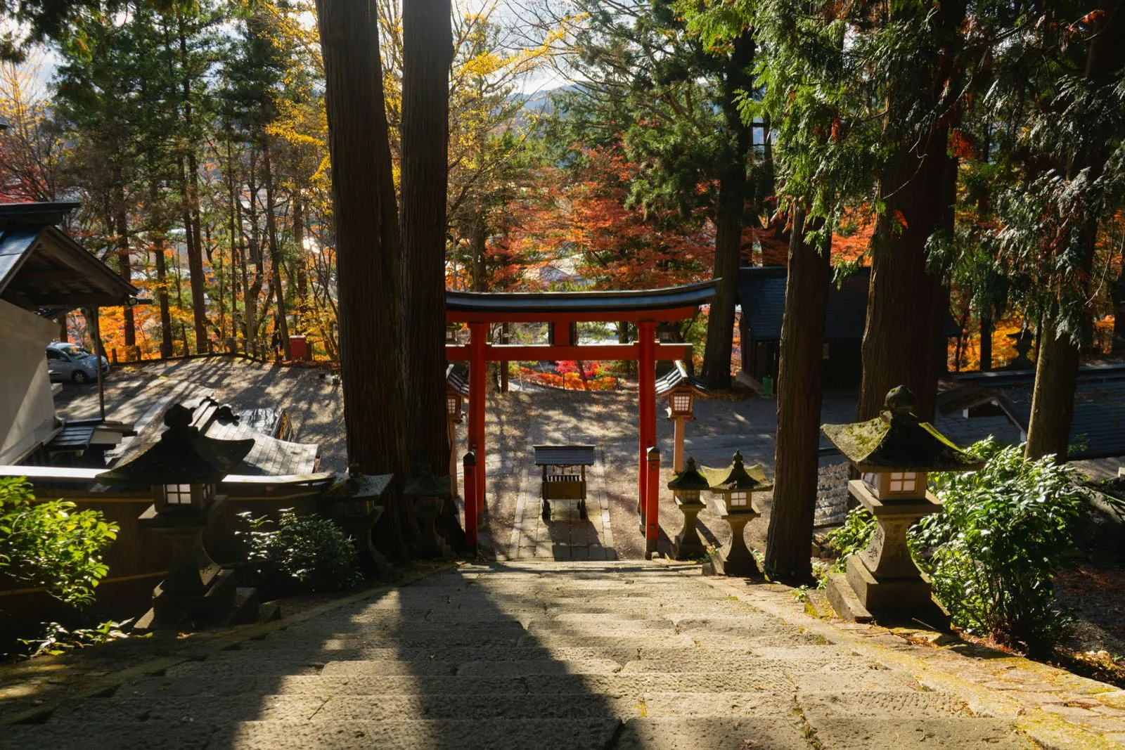 Torii rojo y escalinata de piedra de un santuario de Takayama entre arces de otoño