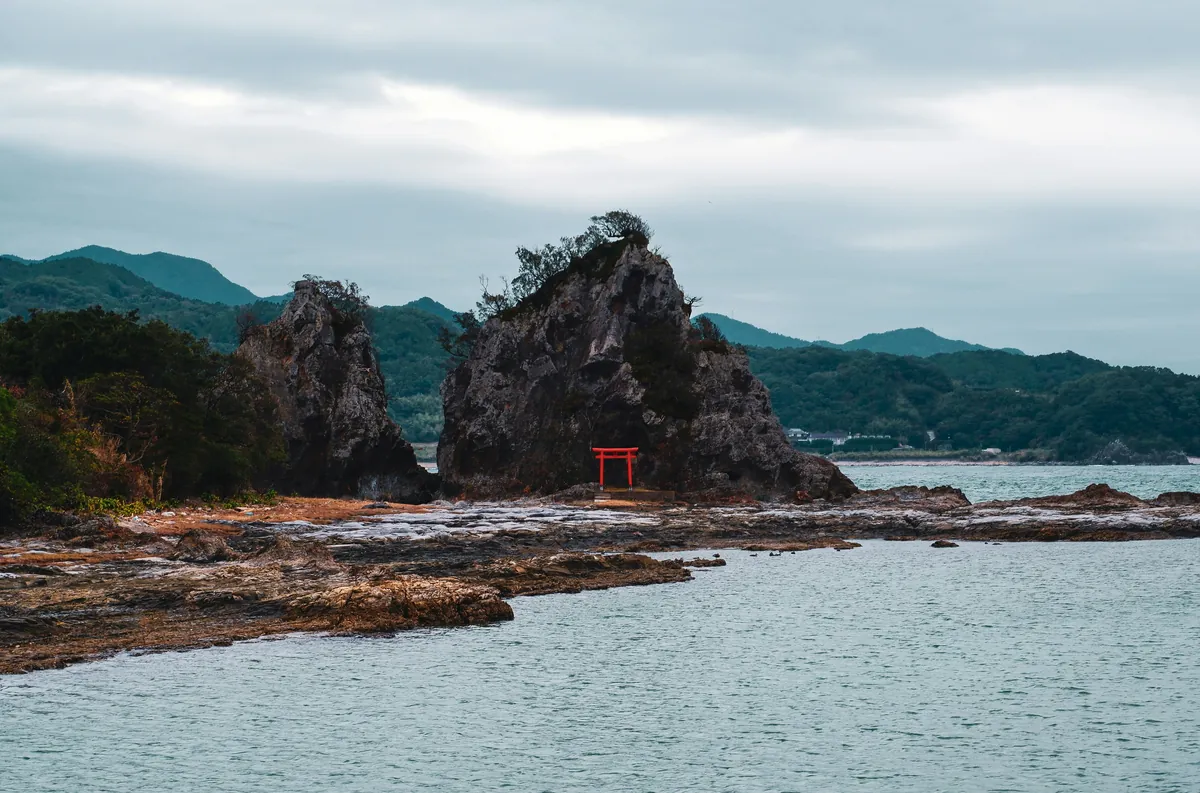 Pequeño torii rojo entre formaciones rocosas frente al mar en la costa de Wakayama